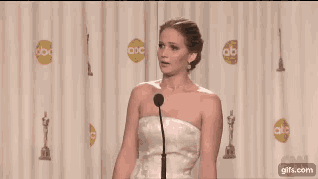a woman in a white strapless dress is standing in front of a microphone .