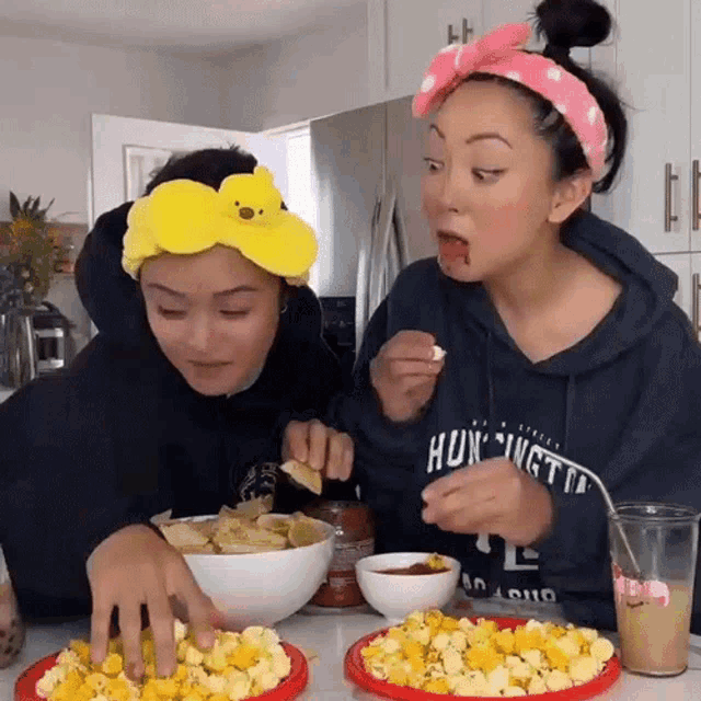 two women are sitting at a table eating popcorn and chips with one wearing a hoodie that says hungry