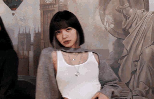 a woman wearing a white tank top and a necklace stands in front of a painting