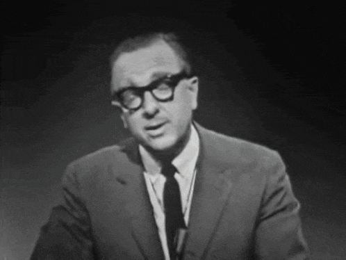a man wearing glasses and a suit stands in front of a microphone