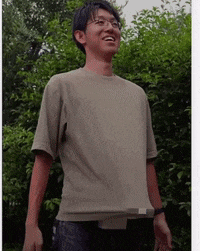 a man wearing glasses and a t-shirt is standing in front of trees .