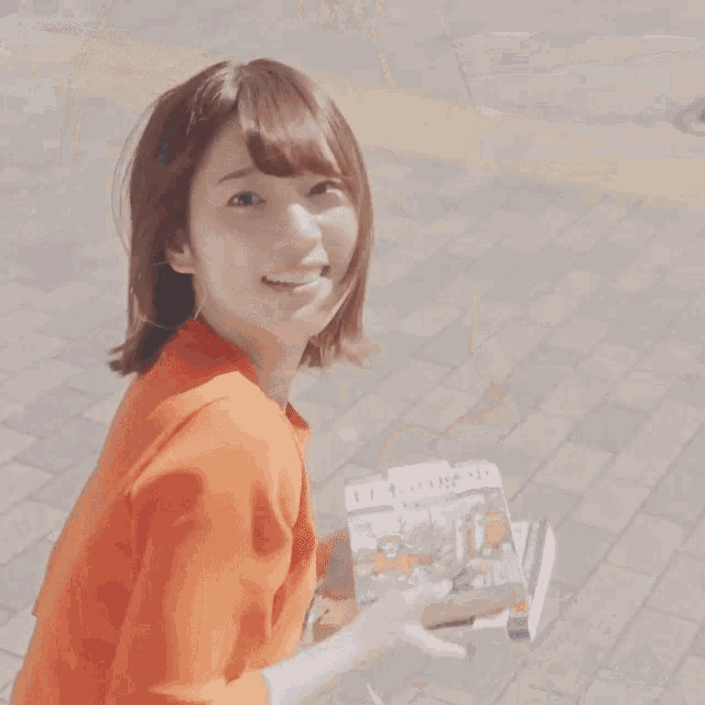 a woman wearing an orange shirt is holding a magazine that says ' ii ' on it