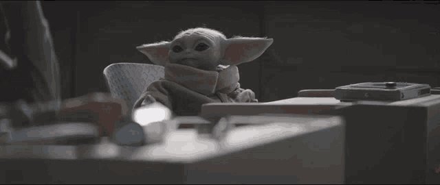 a baby yoda doll is sitting at a table with a remote control .