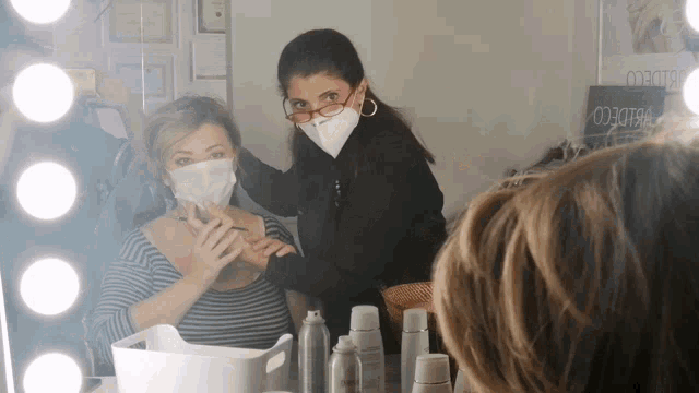 a woman wearing a face mask looks at another woman in front of a mirror