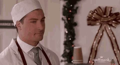 a man in a chef 's hat and apron is standing in front of a christmas tree with his eyes closed .