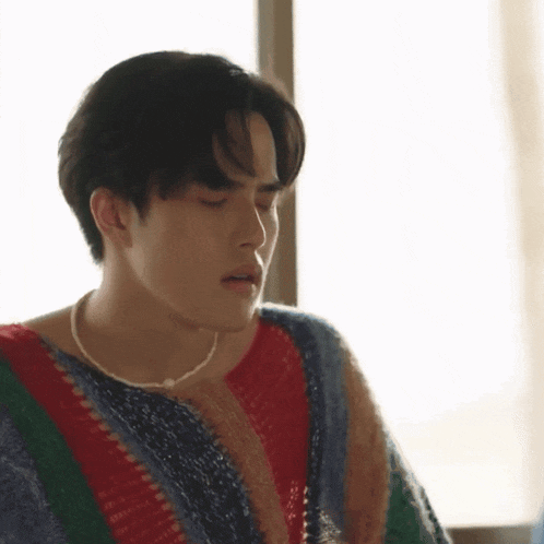 a young man wearing a striped sweater and a pearl necklace .