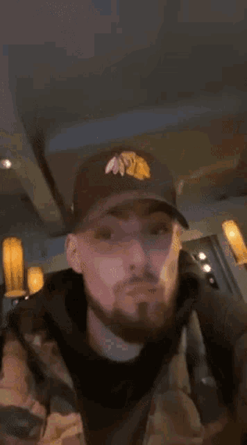 a man with a beard wearing a hat and a jacket is standing in a room .