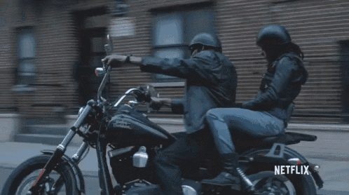 a man and a woman are riding a motorcycle down a street with a netflix logo in the corner