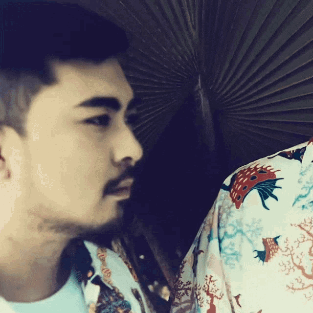 a man with a beard is wearing a blue shirt with a coral pattern