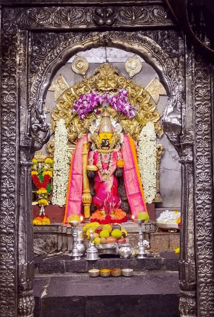 a statue of a woman in a pink dress is surrounded by flowers and offerings