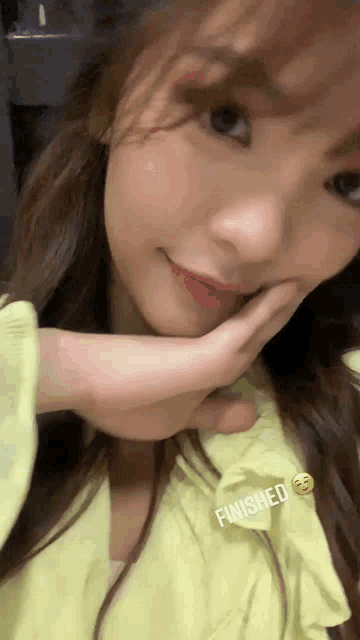 a woman in a yellow shirt is taking a selfie with her hand to her face .