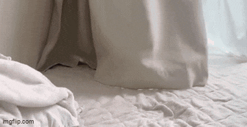 a close up of a bed with white sheets and pillows and a white curtain .