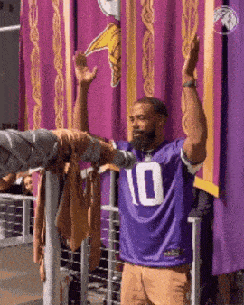 a man in a purple jersey with the number 10 on it is standing in front of purple curtains .