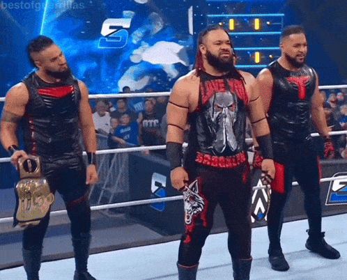three wrestlers are standing in a ring with one wearing a shirt that says i love you