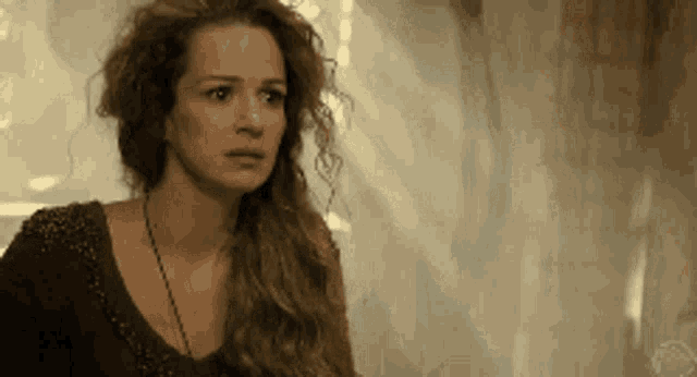 a woman with long curly hair is wearing a brown top and a black necklace