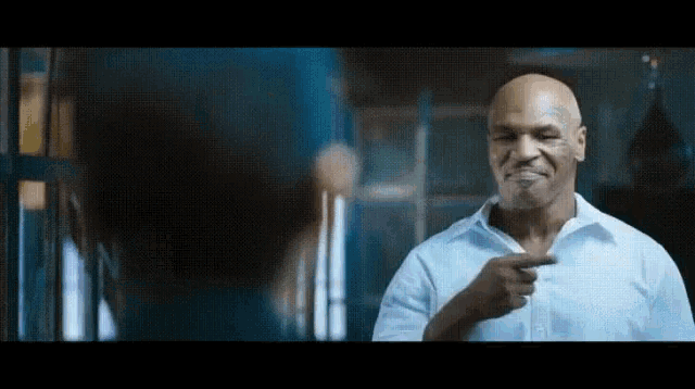 a bald man in a blue shirt is pointing at a woman .