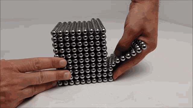 a person is playing with a cube made of metal beads