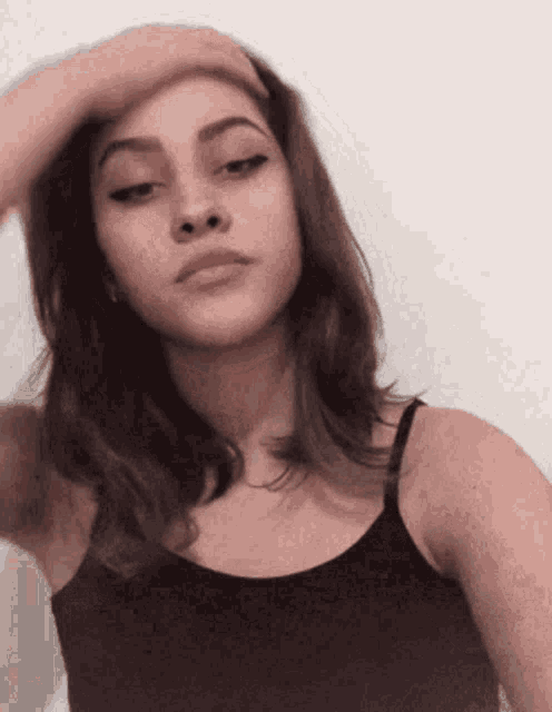 a young woman in a black tank top holds her hand to her forehead