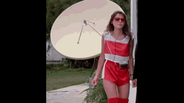 a woman in red shorts is standing in front of a satellite dish