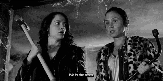 two women are standing next to each other in a room holding a broom and a toothbrush .