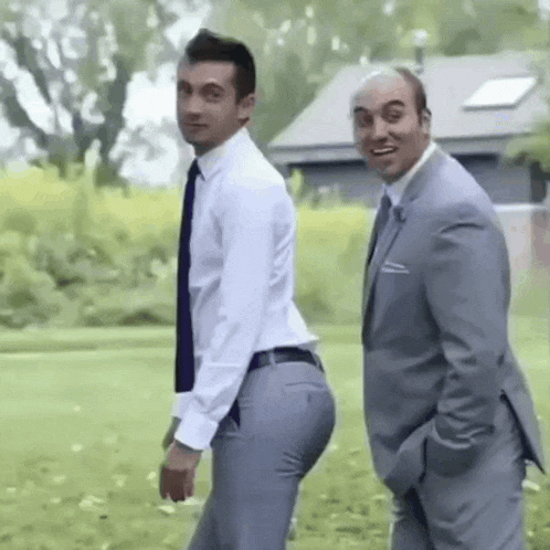 two men in suits and shirts are standing next to each other in a field .