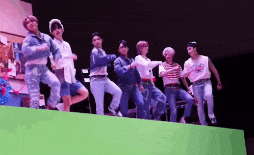 a group of young men are standing on top of a green wall and dancing .