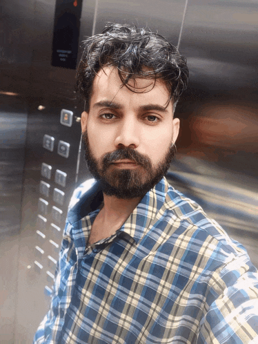 a man with a beard wearing a plaid shirt takes a selfie in an elevator