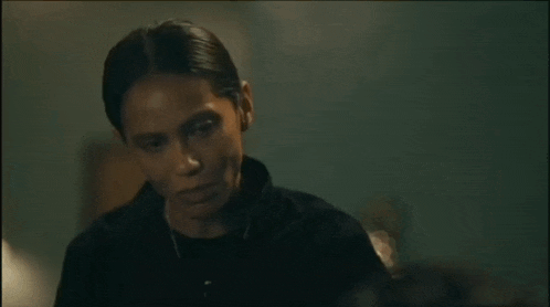a woman in a black shirt is sitting in a dark room looking at something .