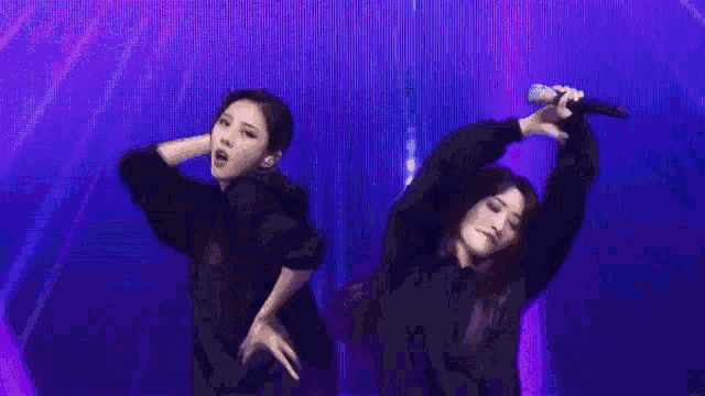 two women are dancing on a stage and one is holding a microphone ..