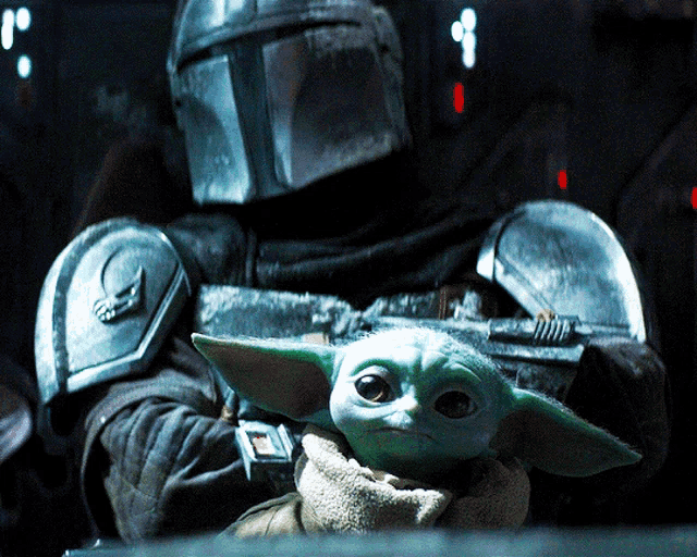 a man in a helmet is holding a baby yoda