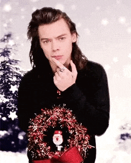 harry styles is wearing a christmas sweater and holding a wreath in his hand .
