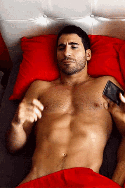 a shirtless man is laying on a bed with red pillows