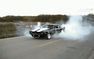 a black car with white stripes is doing a burnout on a road