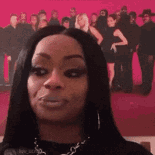a woman is standing in front of a pink background with a group of people standing in the background .