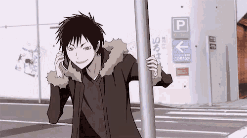 a man is talking on a cell phone while standing next to a pole in front of a parking lot .