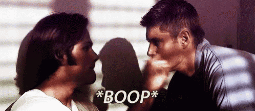 two men are standing next to each other and one of them is giving the other a kiss .