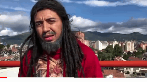 a man with dreadlocks and a beard wearing a red jacket