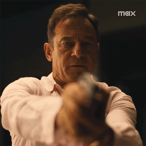 a man in a white shirt is pointing a gun at the camera with a max logo in the background