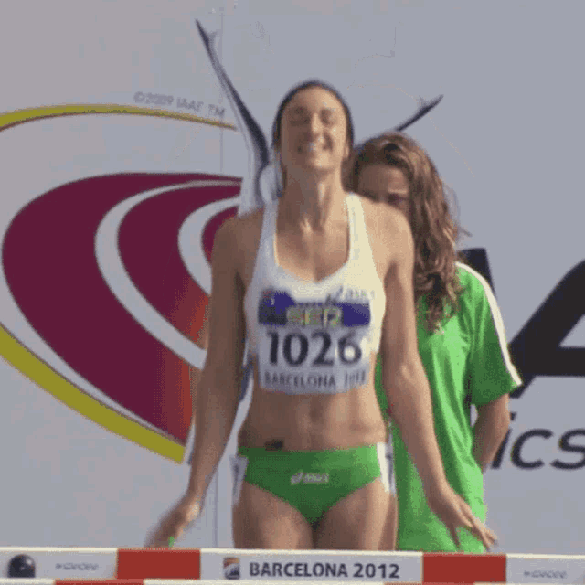 a female runner wearing a white top with the number 1026 on it is jumping over a hurdle