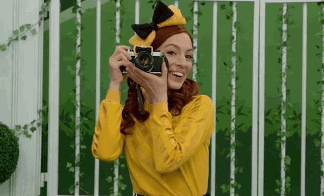 a woman in a yellow top is holding a camera