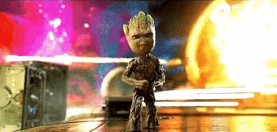 a baby groot is standing on a wooden floor in front of a colorful background .