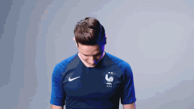 a man wearing a blue shirt with a rooster on it points to his chest