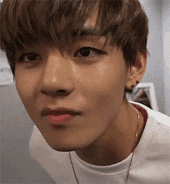 a close up of a young man 's face with a white shirt and a necklace .