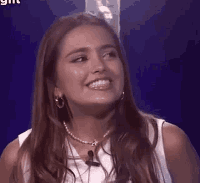 a woman is smiling and looking at the camera while wearing a pearl necklace .