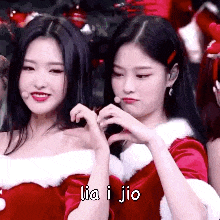 two women are making a heart shape with their hands while wearing santa claus outfits .
