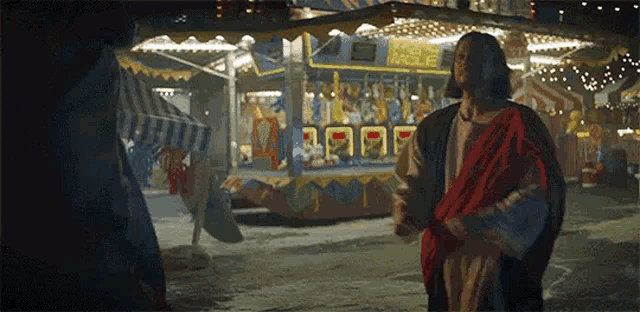 a man dressed as jesus is standing in front of a carnival holding a red scarf .