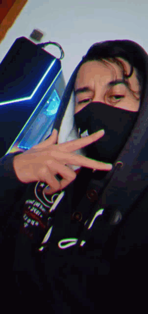 a man wearing a black mask and a black hoodie giving the peace sign