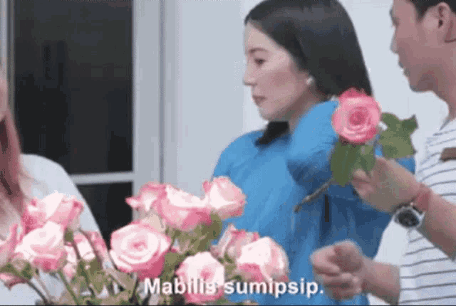a woman in a blue shirt is holding a bouquet of pink roses while a man holds a bouquet of pink roses