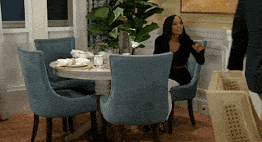 a woman sits at a dining table with blue chairs