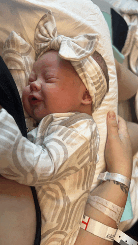 a baby wearing a headband is being held by a person with a hospital wristband
